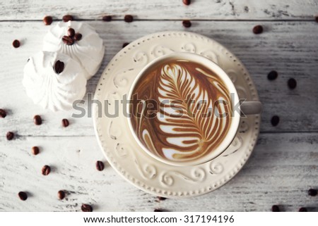 Cup of coffee with beans and zephyr on wooden table, top view