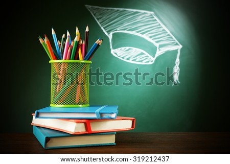 Metal cap of crayons, stack pf books and bachelor hat drawing on blackboard background