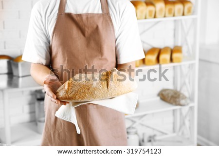 Baker holding freshly baked bread in kitchen of bakery