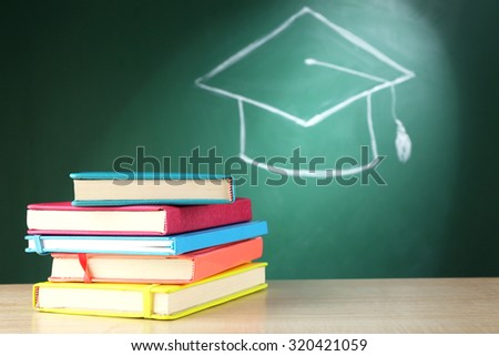 Stack of books and bachelor hat drawing on blackboard background