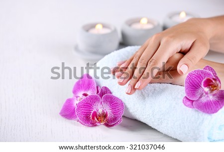 Woman hands with french manicure and orchid flowers on wooden table close-up