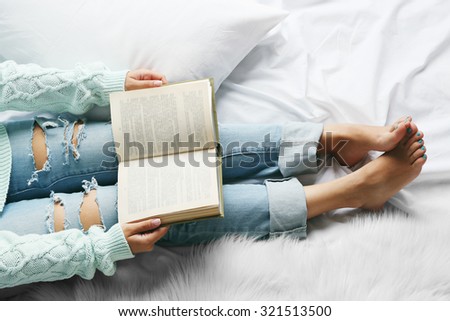 Woman in blue jeans reading book on bed top view point