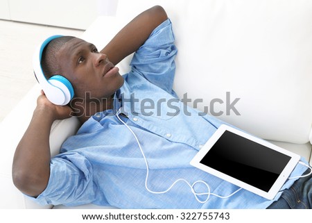 Handsome African American man with headphones and tablet lying on sofa close up