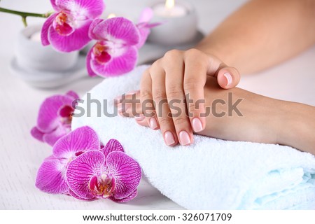 Woman hands with french manicure and orchid flowers on wooden table close-up