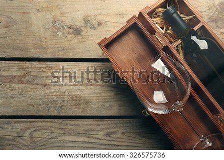 Bottle of wine and empty glass in case on wooden table