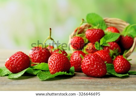 Ripe strawberries with leaves in wicker basket on wooden table on blurred background