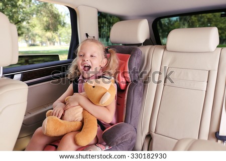 Beautiful happy girl with teddy bear sitting in the car