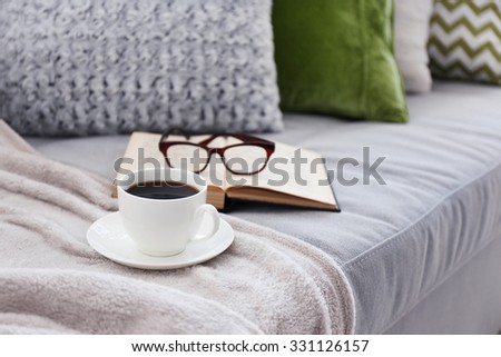 Cup of coffee with book on sofa in room