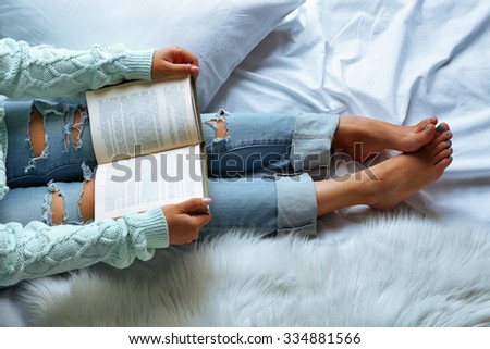 Woman in blue jeans reading book on bed top view point