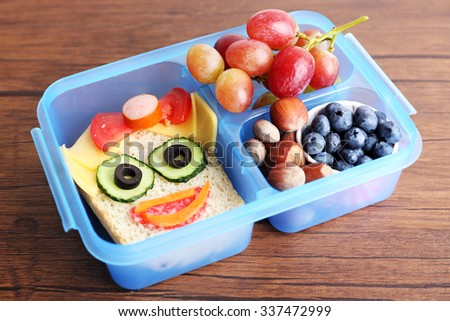 Creative sandwich with fruits and nuts in lunchbox on wooden background