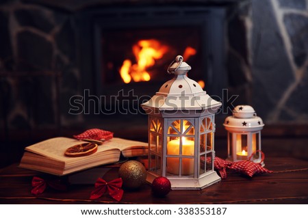 Book and candles on vintage wood table. Fireplace as background