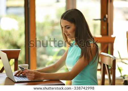 Beautiful young woman with laptop and credit card in cafe