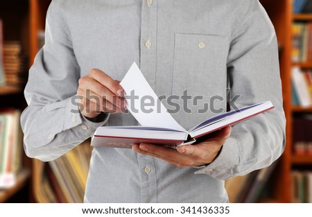 Male hands holding open book on bookshelves background