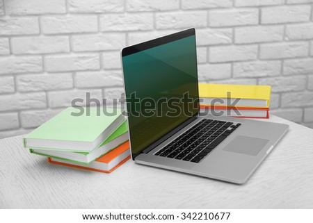 Laptop with books on brick wall background