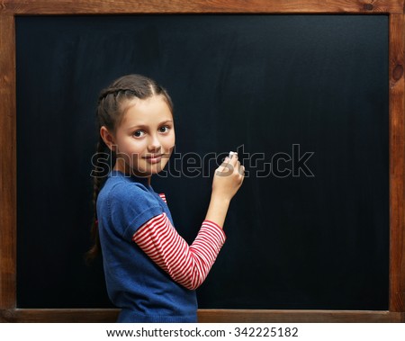 Cute girl posing at the clean blackboard, in the classroom