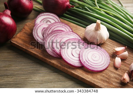 Red onions circles, green onion with garlic on board against wooden background