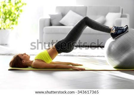 Beautiful young girl doing exercises with fit ball at home