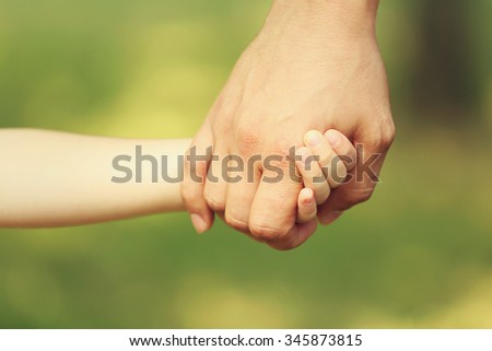 Father\'s hand lead his child daughter outdoors on green defocused background, trust family concept