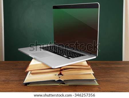 Stack of books with laptop on table in classroom