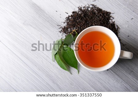 Ceramic cup of tea with scattered tea leaves around on light wooden background