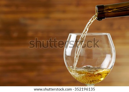 White wine pouring in glass on wooden background