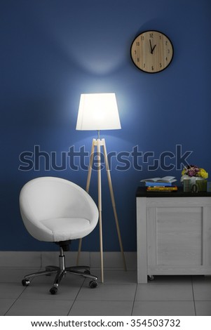 Modern living room with white armchair, commode and floor lamp near blue wall background
