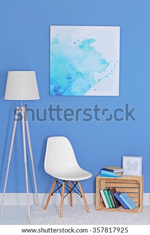 Room design with white floor lamp, chair, bookcase and picture over blue wall
