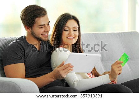 Young happy couple using credit card with tablet at home on light background