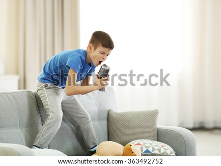 Little boy singing with microphone on a sofa at home