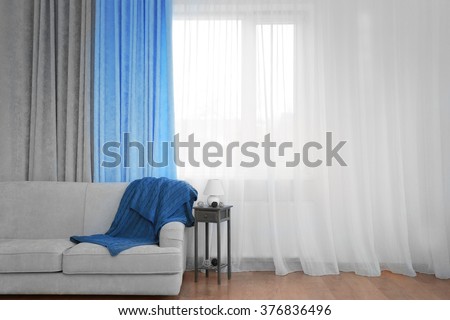 Grey sofa and small table with lamp on curtain background