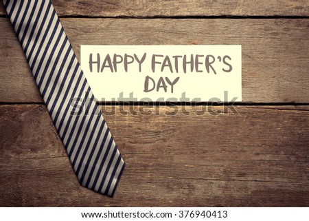 Happy Father's Day inscription with striped tie on wooden background. Greetings and presents