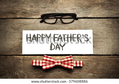 Happy Father\'s Day inscription with red bow tie and glasses on wooden background. Greetings and presents
