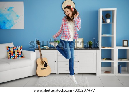 Happy young woman with headphones dancing and listening to music at home