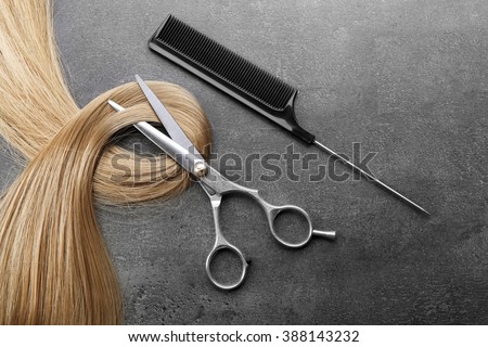 Hairdresser\'s scissors with comb and strand of blonde hair on grey background