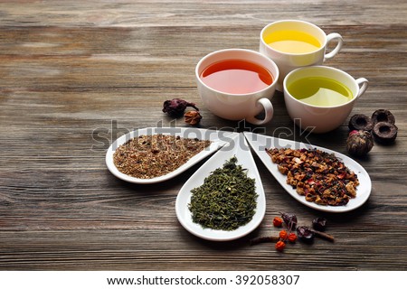 Tea concept. Different kinds of dry tea in ceramic bowls and cups of aromatic tea on wooden background