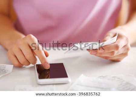 Woman with bills and smart phone at the table. Calculation of costs