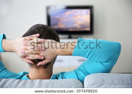 Young handsome man watching TV on a sofa at home