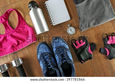 Athlete\'s set with female clothing, equipment, bottle of water and notebook on wooden background