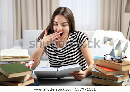 Young tired woman with books yawning at the table