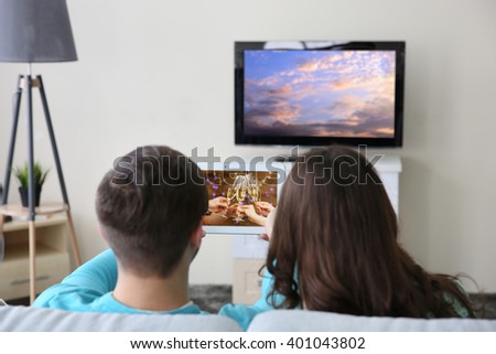 Young couple with tablet watching and taking video from the TV at home