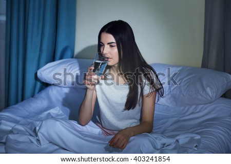 Young woman drinking glass of water in bed at night