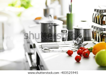 Modern table and electric stove with utensils and vegetables in the kitchen beside window