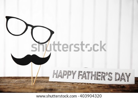 Happy Father\'s Day inscription with paper mustache and glasses on wooden table