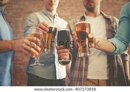 Male group clinking glasses of dark and light beer on brick wall background