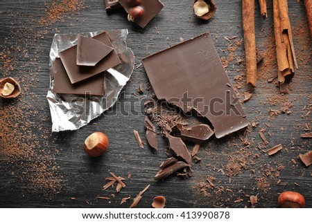 Pieces of chocolate with hazelnuts, cinnamon on black wooden background