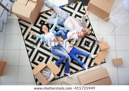 Moving concept. Happy family lying on carpet among cardboard boxes, top view