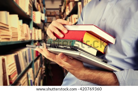 Student holding books and laptop in library