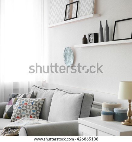 Living room interior, grey couch and shelves with paintings on white wall background