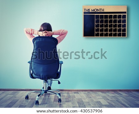 Woman sitting back on the office chair and looking at chalkboard calendar on wall background