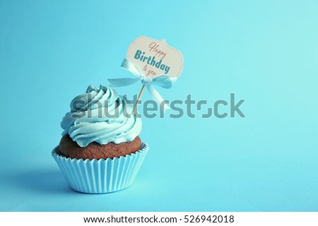Delicious cupcake with greeting card on blue background. Text HAPPY BIRTHDAY TO YOU on card.